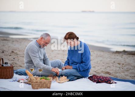 Glückliches Ehepaar, verliebt, sitzt auf einer Decke, trinkt Wein und spielt Schach im Freien am Strand. Stockfoto