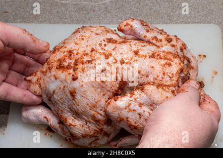 Männliche Hände bedecken rohes ganzes Huhn mit Sauce zum Kochen, Nahaufnahme. Ein Fleischgericht für einen Urlaub kochen. Stockfoto