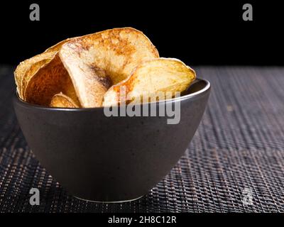 Knusprige goldene hausgemachte Kartoffelchips, serviert in einer dunklen Keramikschale, beliebter salziger Snack oder Beilage. Stockfoto