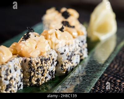 Uramaki Sushi-Rolle mit gehackter Jakobsmuschel und Sesam auf dunklem Hintergrund Stockfoto