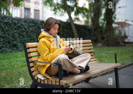 Das Mädchen sitzt auf der Bank und benutzt das Smartphone im Freien in der Stadt. Stockfoto