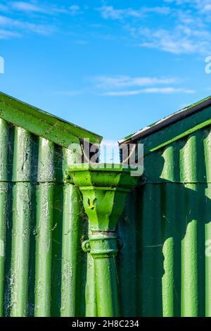 Dachrinnen auf einem grün gestrichenen Vintage Shed, Regenwassertrichter auf alten Vintage-Dachrinnen auf einem grünen Nebengebäude oder Gartenhaus, Wellblechhütte. Stockfoto