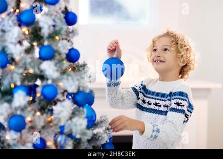 Kinder dekorieren Weihnachten zu Hause. Eröffnungsgeschenke und Geschenke am Weihnachtsmorgen. Blau und weiß Weihnachten Dekoration Thema. Kleines Kind im Pullover Stockfoto