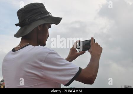 Rückansicht eines jungen Mannes, der bei bewölktem Wetter mit seinem Telefon Landschaftsaufnahmen machte Stockfoto