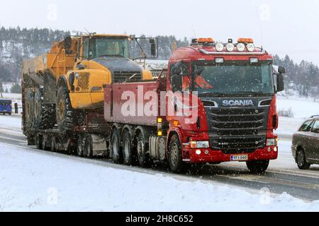 Red Scania R620 Schottertruck schleppt im Winter bei Schneefall den Sattelkipper Volvo A35D auf dem Anhänger entlang der Straße. Salo, Finnland. 15. Januar 2016. Stockfoto