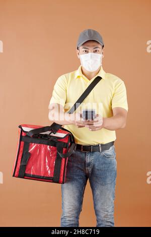 Porträt des Lieferers in medizinischer Maske mit Tasche und Zahlungsterminal Stockfoto