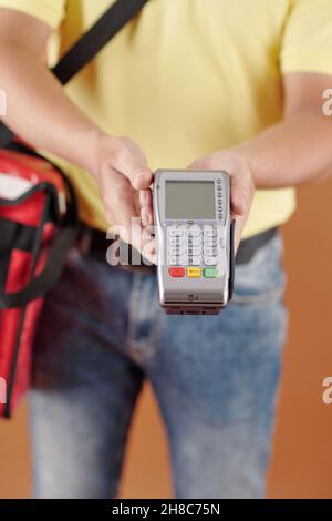Zugeschnittenes Bild des Lieferers, der ein Zahlungsterminal gibt und den Kunden bittet, für den Kauf zu bezahlen Stockfoto