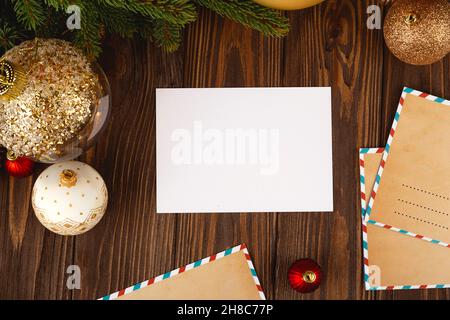 Weihnachtskarte Mockup. Weiße, minimale leere Postkarte auf Holztisch mit festlichen Dekorationen und Bastelbriefen. Stockfoto