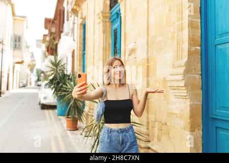 Junge schöne Mädchen in Denim Jeans und Handtasche macht Selfie vor dem Hintergrund der Altstadt von Zypern. Stockfoto