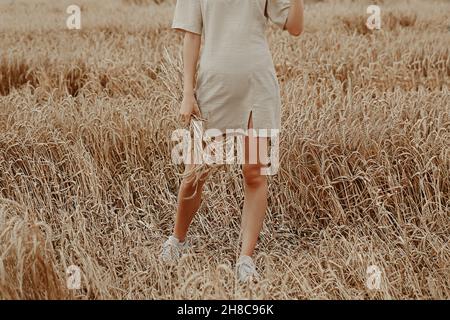 Junge Frau ein junges Mädchen in einem kurzen beigen Kleid steht auf einem Feld mit Weizen.ds in einem Feld mit Weizen. Stockfoto