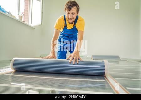 Master installiert einen warmen Fußboden im Raum. Installation der Fußbodenheizung Stockfoto