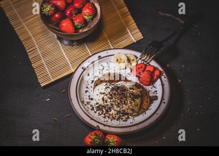 Nahaufnahme von Bananenpfannkuchen mit Vanilleeis mit Fruchtscheiben auf der Seite Stockfoto