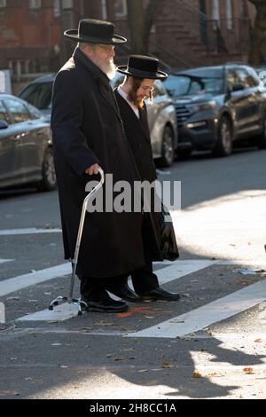 Ein orthodoxer jüdischer Mann mit einem Stock überquert an einem Herbsttag mit seinem Enkel die Straße Stockfoto