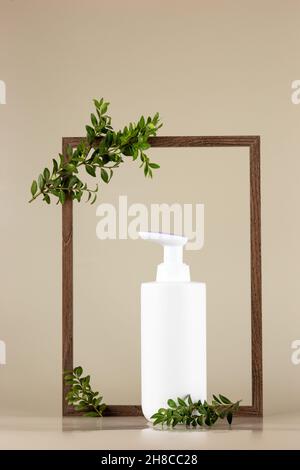 Weiße Kosmetikflasche, steht in einem leeren Holzrahmen mit Ästen einer grünen Pflanze Stockfoto