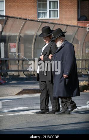 Ein orthodoxer jüdischer Mann überquert die Straße mit Hilfe eines jüngeren Mannes, möglicherweise seines Enkels. An einem Herbsttag. In Williamsburg, Brooklyn, New Yor. Stockfoto