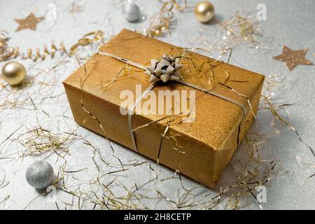 Glänzende goldene Geschenkbox auf silbernem Glitzer-Hintergrund mit Konfetti Stockfoto