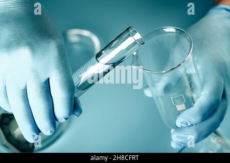 Arzthände in medizinischen Handschuhen mit Kolben. Abstrakter medizinischer Hintergrund im Labor. petrischalen, Reagenzgläser Stockfoto