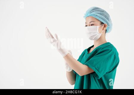 Junge Krankenschwester in einem medizinischen Hut und einer Schutzmaske, die Gummihandschuhe anziehen, wenn sie sich für die Arbeit bereit machen Stockfoto