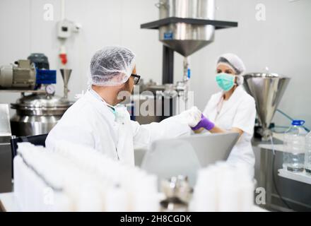 Junger erfolgreicher Technologe, der mit seinem Assistenten Gesichtspflegecremes macht. Stockfoto