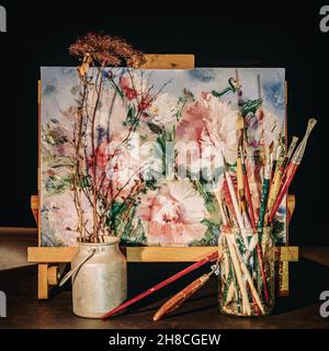 Staffelei, Bild mit Blumen, Malpinsel auf dunklem Hintergrund. Hobby-Konzept Stockfoto