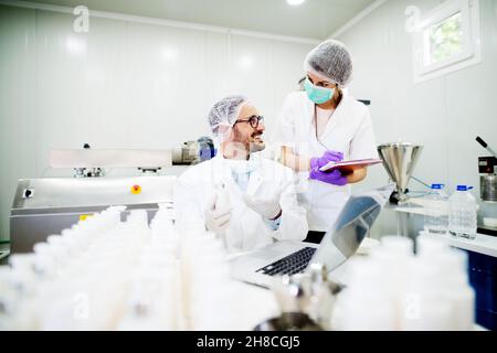 Junger erfolgreicher Technologe, der mit seinem Assistenten Gesichtspflegecremes macht. Stockfoto