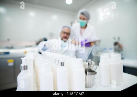 Junger erfolgreicher Technologe, der mit seinem Assistenten Gesichtspflegecremes macht. Arbeiten mit High-Tech-Geräten. Creme Tube im Fokus. Stockfoto