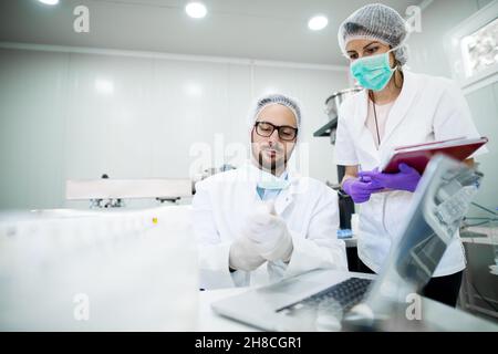 Junger erfolgreicher Technologe, der mit seinem Assistenten Gesichtspflegecremes macht. Arbeiten mit High-Tech-Geräten. Stockfoto