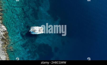 Schöner Segel-Katamaran neben der Insel vor Anker. Luftaufnahme der Yacht im klaren türkisfarbenen Meerwasser. Yachting und Reisekonzept Stockfoto