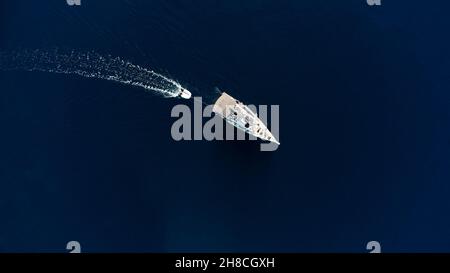 Private Yacht, mit einem aufblasbaren Boot an der Rückseite gebunden, segelt auf dem blauen Meer. Luftdrohne, extrem breites Foto von oben nach unten Stockfoto