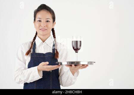 Positive Kellnerin im Restaurant, die dem Gast ein Glas guten Rotweins serviert, isoliert auf Weiß Stockfoto