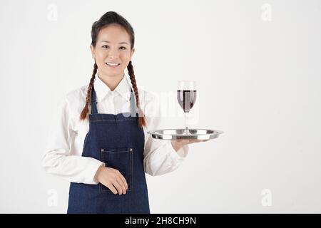 Porträt einer ziemlich lächelnden Kellnerin, die ein Glas Wein auf einem Metalltablett hält Stockfoto