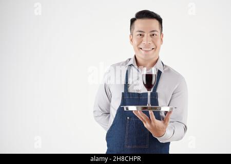 Porträt eines lächelnden, gastfreundlichen Kellners, der ein Glas Rotwein serviert, isoliert auf Weiß Stockfoto