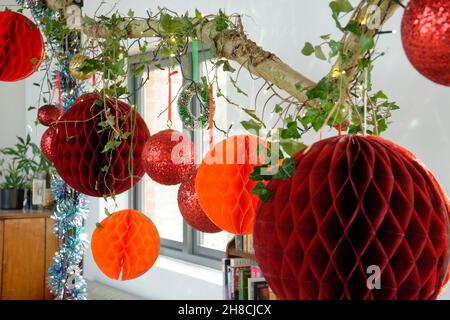 Weihnachtskugeldekorationen, die an einem Holzzweig hängen und mit Efeu und Lichterketten geschmückt sind. Stockfoto