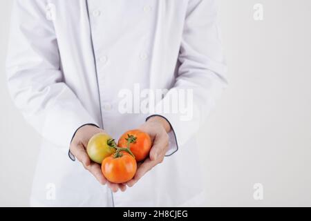 Nahaufnahme des Küchenchefs in weißer Uniform mit frischen Tomaten Stockfoto