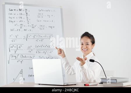 Porträt einer lächelnden jungen Frau, die online Mathematik unterrichtet und auf ein Whiteboard mit Formeln zeigt Stockfoto