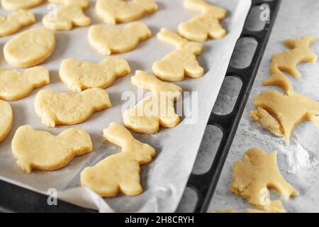 Bereit zum Backen von Cookies, die in Form von Kaninchen, Ei und Huhn auf Pergamentpapier geschnitten werden Stockfoto