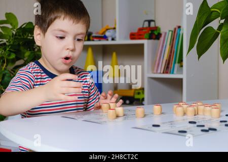 Ein 4-jähriger Junge spielt loto und studiert Zahlen anhand eines Brettspiels. Stockfoto