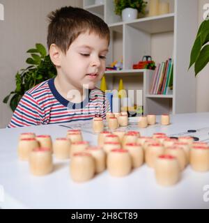 Ein 4-jähriger Junge spielt loto und studiert Zahlen anhand eines Brettspiels. Stockfoto