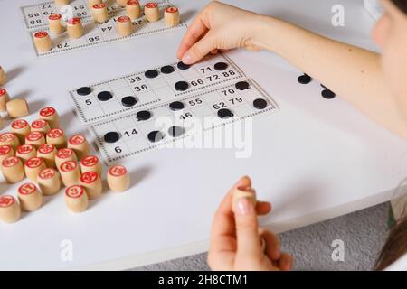 Eine Frau spielt ein Tischspiel des russischen Lotto, schließt Karten mit Zahlen mit Chips. Stockfoto