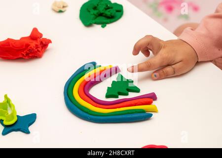 Mädchen spielt Teig. Mädchen macht Regenbogen mit Teig auf weißem Hintergrund. Verschiedene Formen mit Teig herstellen. Stockfoto