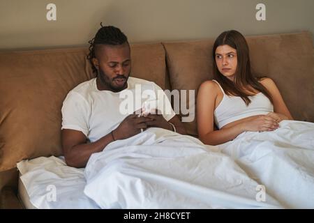 Traurige Frau starrte den Mann an und konzentrierte sich auf sein Handy Stockfoto