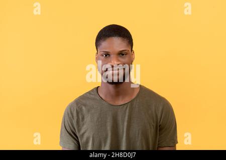 Hübscher afroamerikanischer bärtiger Mann, der die Kamera anschaut und lächelt, trägt ein T-Shirt und posiert auf gelbem Hintergrund Stockfoto