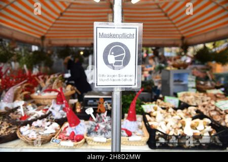 29. November 2021, Bayern, München: Am Viktualienmarkt hängt ein Schild mit der Aufschrift „Maskenpflicht“ an einem Verkaufsstand, an dem unter anderem Weihnachtsartikel angeboten werden. Foto: Felix Hörhager/dpa Stockfoto