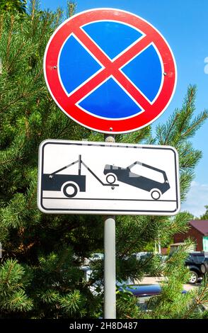 Straßenschilder „Stopp verboten“ und „Abschleppwagen funktioniert“ im Sommer vor dem Hintergrund grüner Bäume auf der Straße. Evakuierung am Abschleppwagen Stockfoto