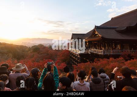 Besucher fotografieren den buddhistischen Tempel Kiyomizu-dera in Kyoto, der von Herbstblättern umgeben ist. Stockfoto