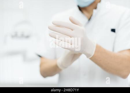 Nahaufnahme Arzt Hände in Handschuhe. Herstellung von Gummihandschuhen, menschliche Hand trägt Latexhandschuhe. Arzt, der Nitril-Schutzhandschuhe anlegt Stockfoto