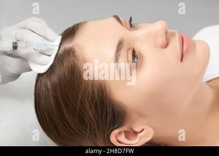 Seitenansicht der Kosmetikerin in weißen Gummihandschuhen tun Injektion für Haare in professionellen Schönheitssalon. Konzept von speziellen Verfahren zur Verbesserung der Haarkondition. Stockfoto