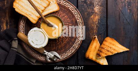 Kondensmilch oder verdampfte Milch in offener Dose auf dunklem alten Holztisch. Rustikaler Stil.Draufsicht. Stockfoto