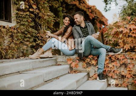 Schönes junges Paar, das an einem Herbsttag mit Mobiltelefonen auf der Außentreppe sitzt Stockfoto