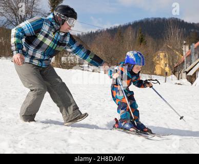 Der Junge lernt während des Winterurlaubs in verschneiten Bergen an sonnigen, kalten Tagen mit seinem Vater Ski zu fahren. Winter aktiv Spaziergänge mit Kindern. Saisonale Freuden, Stockfoto